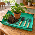 Green repotting mat with snap corners forming a tray on a kitchen table, with a pothos being repotted and three mini garden tools